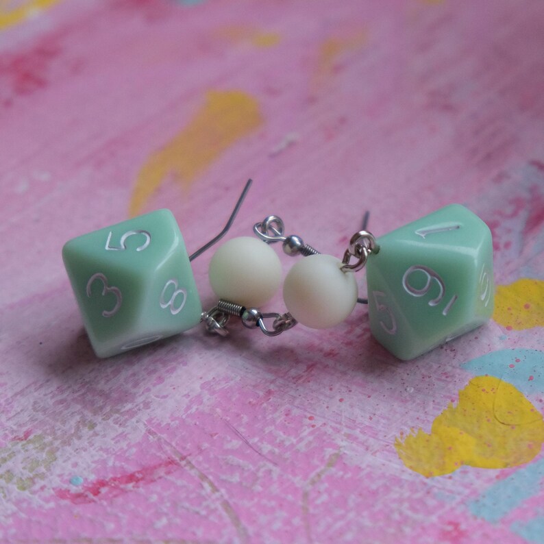 May include: A pair of green dice earrings with white numbers. Each earring has a white pearl bead on the wire.