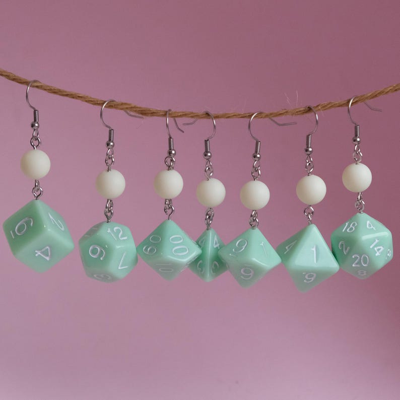 May include: A set of six green dice earrings with white numbers. Each earring has a white bead above the dice.