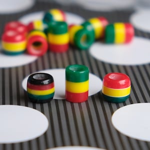 Peut inclure: Un ensemble de perles rondes colorées avec un schéma de couleurs vert, jaune et rouge. Les perles sont disposées en motif sur une surface rayée gris et blanc.