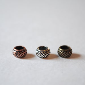 May include: Three metal beads with a chevron pattern. The beads are copper, silver, and gold.
