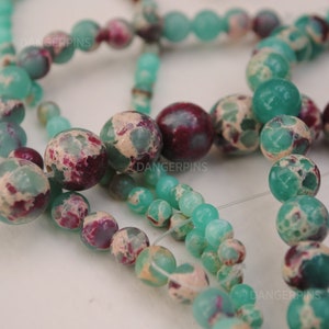 May include: A strand of green and white marbled beads with red and white marbled beads. The beads are round and have a speckled appearance.