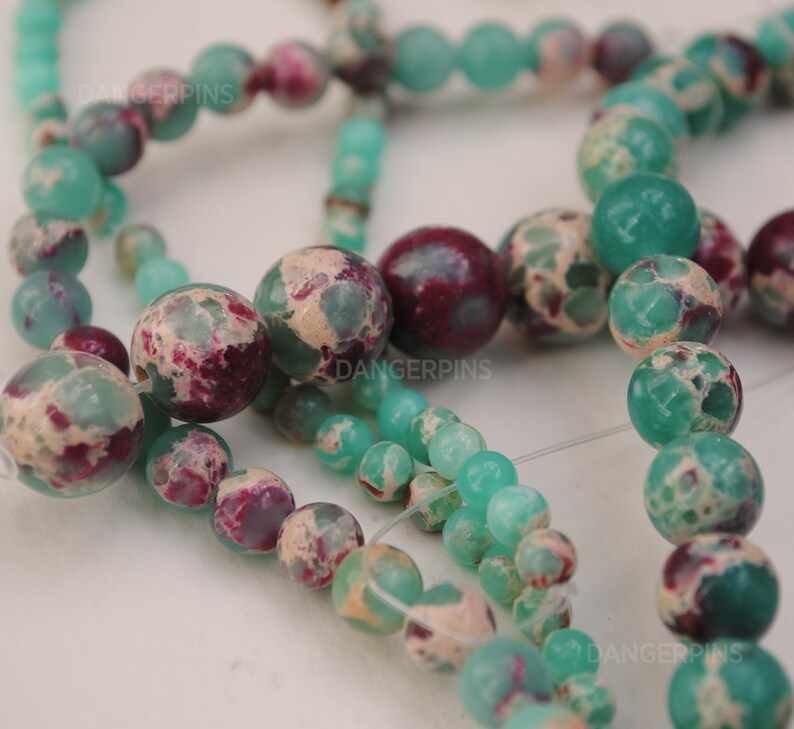 May include: A strand of green and white marbled beads with red and white marbled beads. The beads are round and have a speckled appearance.