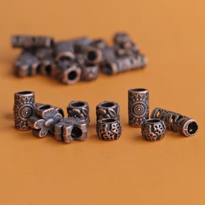 May include: A collection of antique bronze-colored beads with various designs. The beads include cylindrical, floral, and spherical shapes, with intricate patterns. The beads are scattered on a solid orange background, creating a visually appealing arrangement for jewelry making.