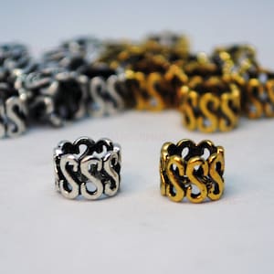 May include: Two silver and gold hair rings with a decorative design of interlocking S shapes.