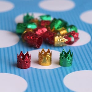 May include: Three small, gold, red, and green crown-shaped metal beads. The beads are on a blue and white polka dot background.