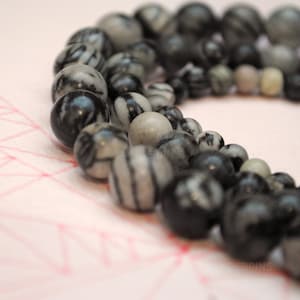Peut inclure: Un collier de perles rayées noires et blanches. Les perles sont rondes et ont une finition lisse et polie.