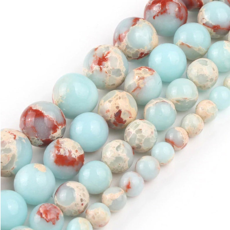 May include: A strand of round, blue and white marbled beads with red accents. The beads are smooth and polished.