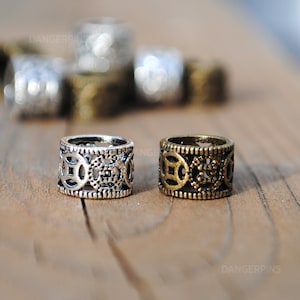 May include: Two metal hair beads with a circular design. One bead is silver and the other is gold.