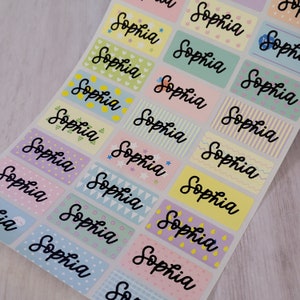 May include: A sheet of colorful rectangular stickers with the name "Sophia" written in cursive on each sticker. The stickers have different patterns including stars, lemons, hearts, and stripes.