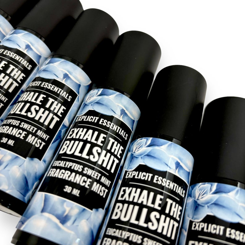 Puede incluir: Varias botellas de bruma perfumada con tapas negras dispuestas en diagonal. Las etiquetas dicen "EXHALE THE BULLSHIT" y "Eucalyptus Sweet Mint Fragrance Mist". Las botellas tienen un dise&ntilde;o floral azul y est&aacute;n etiquetadas como "Explicit Essentials."