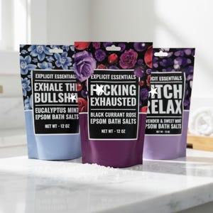 May include: Three pouches of Explicit Essentials Epsom bath salts, each 12 oz. The blue pouch features eucalyptus mint, the purple pouch features black currant rose, and the lavender pouch features lavender and sweet mint, all with floral graphics.