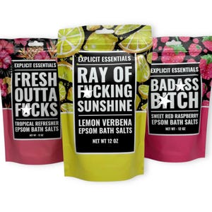 May include: Three colorful bags of Epsom bath salts with bold text. The bags are pink, yellow, and pink again. The text on the bags reads: "FRESH OUTTA FUCKS", "RAY OF FUCKING SUNSHINE", and "BADASS BITCH". Each bag contains 12 oz of product.