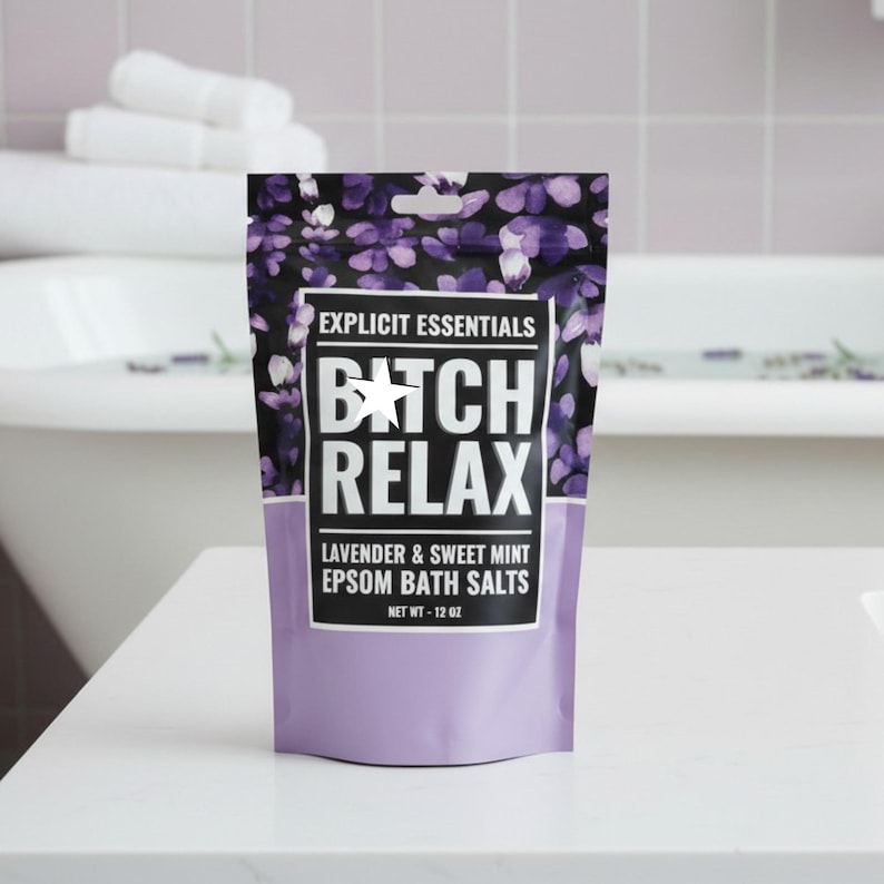 Op de afbeelding: Een stazak met Explicit Essentials Epsom-badzout in lavendel en zoete munt. De verpakking heeft een paars bloemenpatroon, een wit label met de zwarte tekst BITCH RELAX en een nettogewicht van 12 oz dat op de voorzijde is gedrukt.