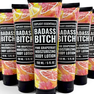 May include: A group of five squeeze tubes of Explicit Essentials Badass Bitch Pink Grapefruit Moisturizing Body Lotion. Each tube features a black cap, a black label with white text, and a background pattern of pink grapefruit slices and flowers.