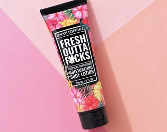 May include: A squeeze tube of moisturizing body lotion featuring a tropical floral pattern with pink, red, and yellow hibiscus flowers and green palm leaves. The black label displays the text Explicit Essentials, Fresh Outta Fucks, Tropical Refresher, Moisturizing Body Lotion, and 150 ml / 5 fl oz.