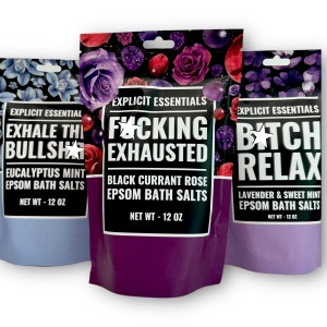 May include: Three bags of bath salts with colorful floral designs and humorous phrases. The first bag is blue with the phrase "Exhale the Bullsh*t" and "Eucalyptus Mint Epsom Bath Salts". The second bag is purple with the phrase "F*cking Exhausted" and "Black Currant Rose Epsom Bath Salts". The third bag is lavender with the phrase "Bitch Relax" and "Lavender & Sweet Mint Epsom Bath Salts". Each bag is 12 oz.