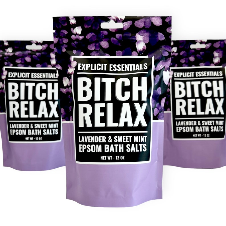 Op de afbeelding: Drie staande zakjes met Explicit Essentials Bitch Relax Lavendel & Zoete Munt Epsom badzout. Elke zak heeft een zwart en paars bloemenpatroon aan de bovenkant, een wit label met dikke zwarte tekst en een lichtpaarse onderkant, netto gewicht 340g.