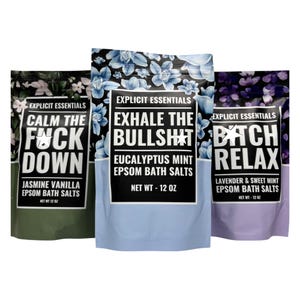 May include: Three bags of Explicit Essentials Epsom bath salts. The bags are green, blue, and purple, each with a floral pattern. Text on the bags reads "Calm the F*ck Down," "Exhale the Bullsh*t," and "B*tch Relax." Each bag contains 12 oz of bath salts.