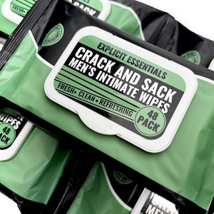 May include: A stack of black and green packages of intimate wipes. The packages have a white label with the text "CRACK AND SACK MEN'S INTIMATE WIPES" in bold black letters. The label also includes the words "FRESH CLEAN REFRESHING" and "48 PACK".
