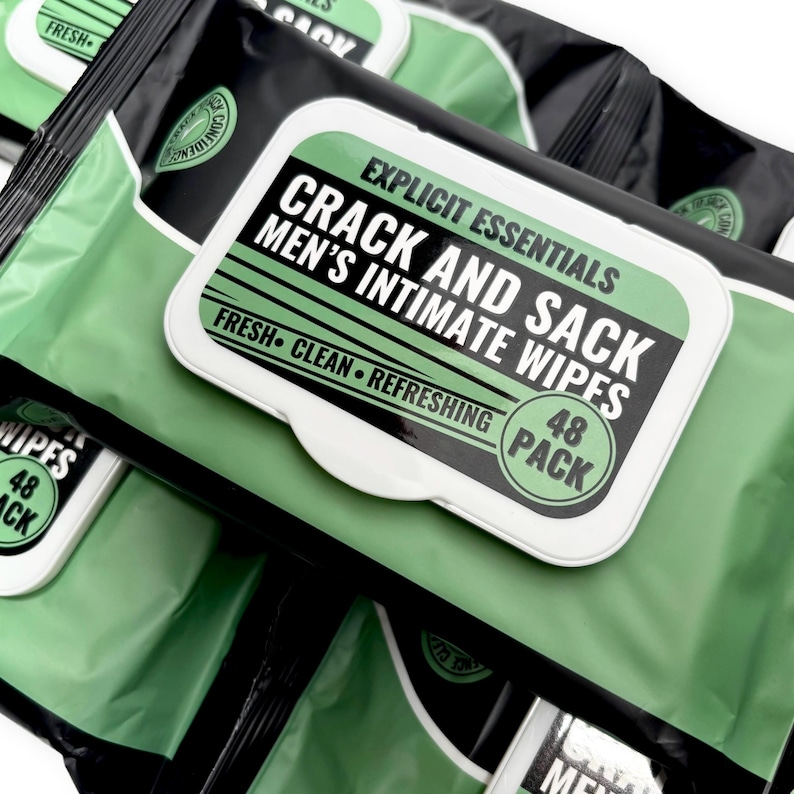 May include: A stack of black and green packages of intimate wipes. The packages have a white label with the text "CRACK AND SACK MEN'S INTIMATE WIPES" in bold black letters. The label also includes the words "FRESH CLEAN REFRESHING" and "48 PACK".