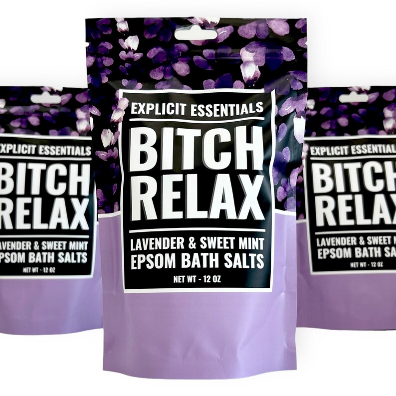 Op de afbeelding: Drie zakjes Explicit Essentials Bitch Relax Epsom-badzout met lavendel en zoete munt. Elk zakje heeft een zwarte bovenkant met paarse bloemmotieven, een wit centraal label met zwarte tekst en een effen lichtpaarse onderkant.