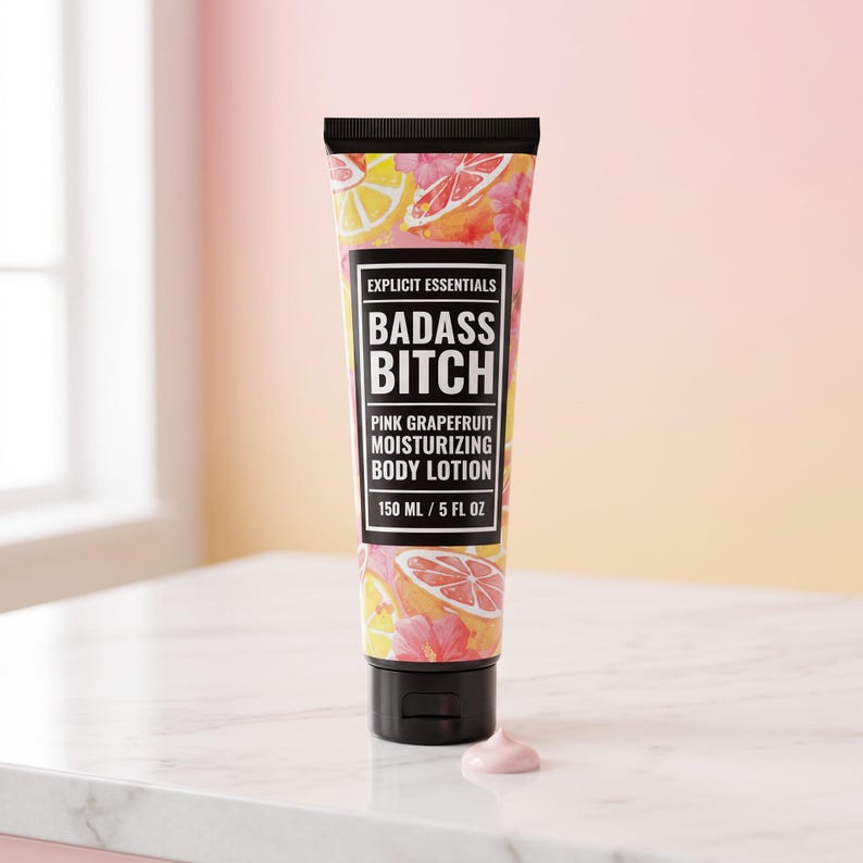 May include: A squeeze tube of Explicit Essentials Badass Bitch pink grapefruit moisturizing body lotion. The tube features a black label with white text and a colorful citrus and floral pattern. It contains 150 ml / 5 fl oz of product.
