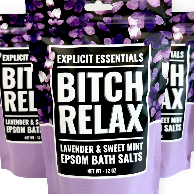 Op de afbeelding: Een staande zak met Explicit Essentials Bitch Relax lavendel en zoete munt Epsom badzout. De verpakking heeft een zwarte achtergrond met paarse bloemillustraties, witte tekst en een nettogewicht van 12 oz op de voorzijde.