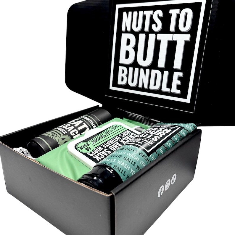 May include: A black gift box labelled "Nuts to Butt Bundle" contains personal care products. Items include a tube of body wash, a container of powder, and a pack of intimate wipes. The box has a white interior.