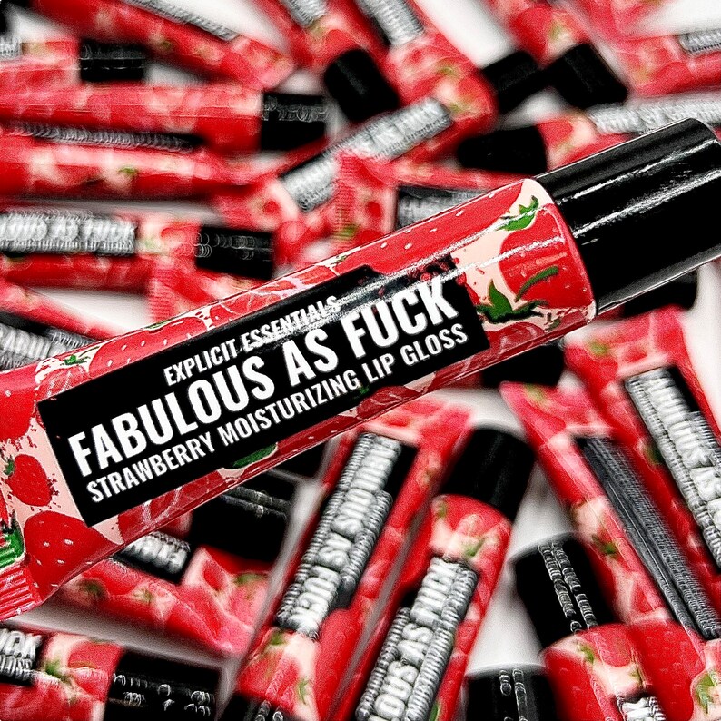 May include: A close-up of a red and black lip gloss tube with the text "EXPLICIT ESSENTIALS FABULOUS AS FUCK STRAWBERRY MOISTURIZING LIP GLOSS".