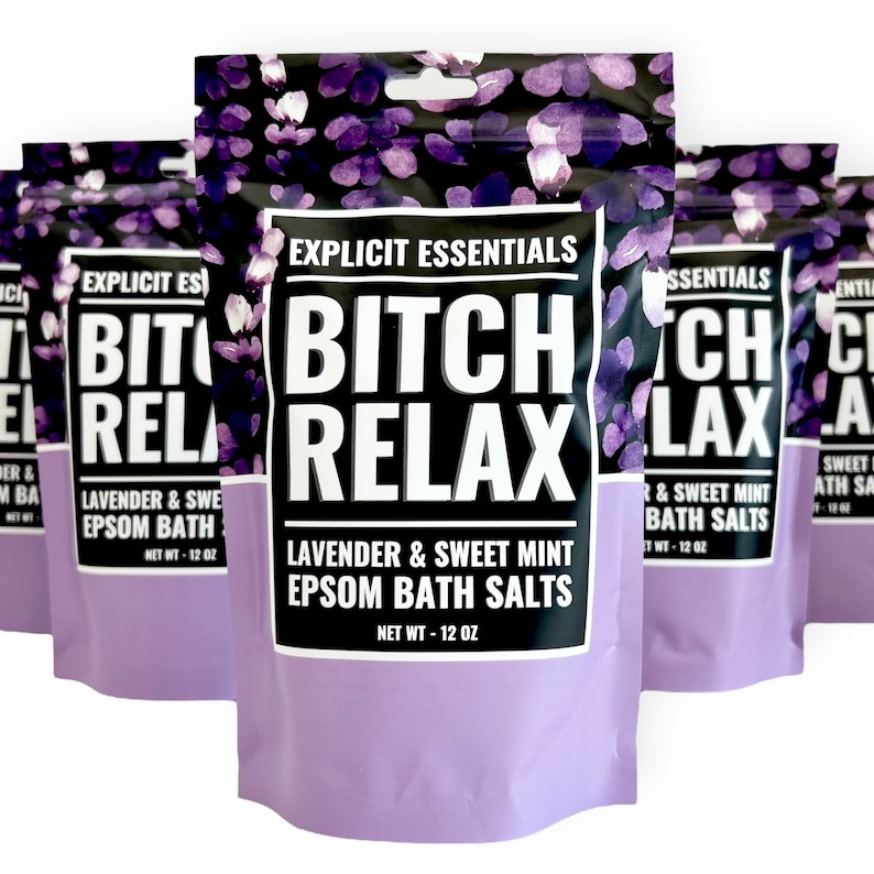 Op de afbeelding: Meerdere zakjes Explicit Essentials Bitch Relax Lavendel & Zoete Munt Epsom Badzout. Elk zakje heeft een zwart en paars bloemenpatroon, een wit label met dikke zwarte tekst en een nettogewicht van 340 gram per verpakking.