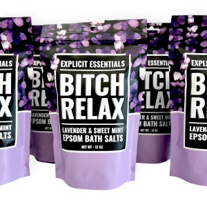 Op de afbeelding: Een staande zak met Epsom-badzout met lavendel en zoete munt, voorzien van een zwart en paars bloemenpatroon. Het etiket bevat de tekst Explicit Essentials, Bitch Relax, Lavender & Sweet Mint Epsom Bath Salts en Net Wt - 12 oz.