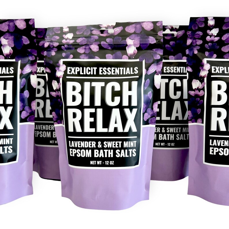 Op de afbeelding: Een staande zak met Epsom-badzout met lavendel en zoete munt, voorzien van een zwart en paars bloemenpatroon. Het etiket bevat de tekst Explicit Essentials, Bitch Relax, Lavender & Sweet Mint Epsom Bath Salts en Net Wt - 12 oz.
