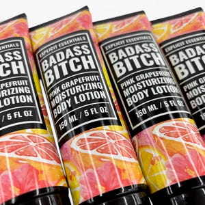 May include: Four tubes of Explicit Essentials Badass Bitch pink grapefruit moisturizing body lotion. Each tube features a black label with white text and a vibrant graphic of pink hibiscus flowers and sliced grapefruit. Each contains 150 ml / 5 fl oz.