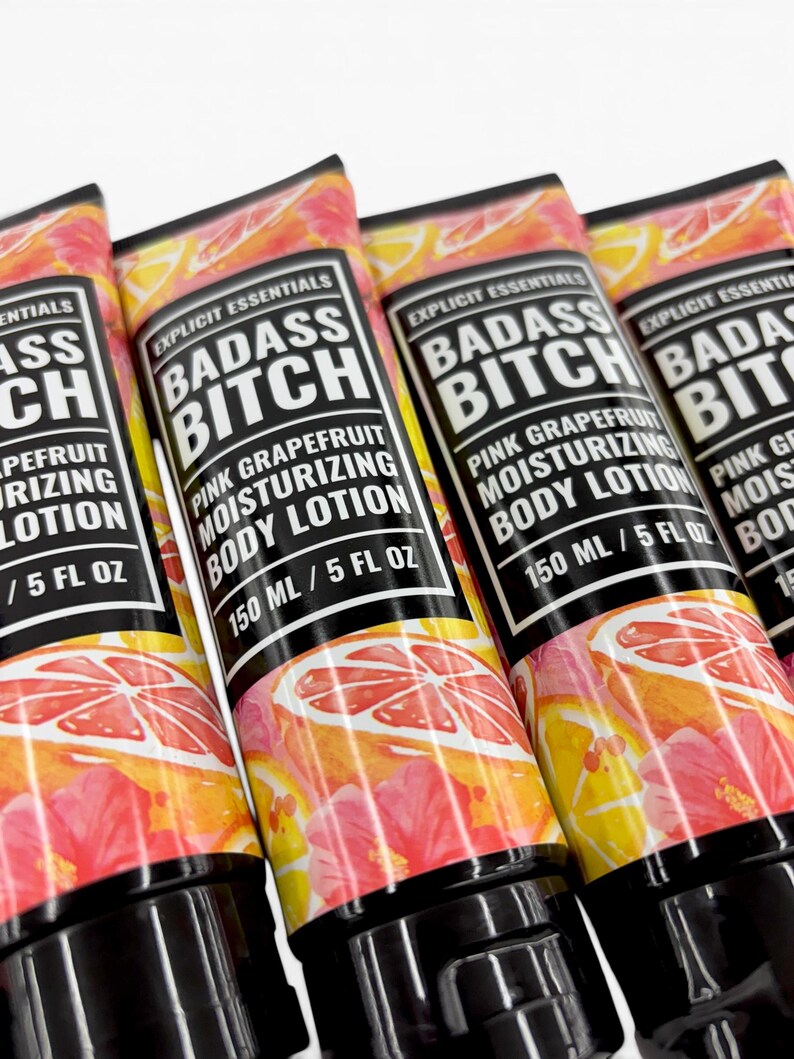 May include: Four tubes of Explicit Essentials Badass Bitch pink grapefruit moisturizing body lotion. Each tube features a black label with white text and a vibrant graphic of pink hibiscus flowers and sliced grapefruit. Each contains 150 ml / 5 fl oz.