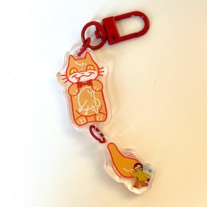 Puede incluir: Un llavero de acrílico transparente con un gato naranja de dibujos animados que sostiene un reloj. El gato lleva una pajarita roja. El llavero tiene un anillo de metal rojo y una pieza separada de acrílico transparente con una persona de dibujos animados que huye de la cola del gato.
