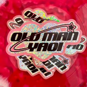 Peut inclure: Autocollant en forme de c&oelig;ur rose avec des paillettes et un design noir et blanc. L'autocollant dit "Old Man Yaoi" et a une &eacute;toile et une queue de com&egrave;te.