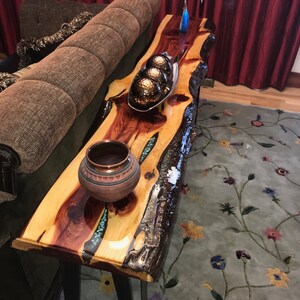 May include: A rustic wooden table with a live edge top and black metal legs. The table is decorated with a bowl of decorative balls and a small pottery vase. The table is sitting on a rug with a floral pattern.