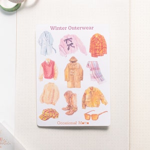 May include: A sheet of stickers featuring illustrations of winter outerwear, including a coat, sweater, scarf, hat, boots, and sunglasses. The sheet is titled "Winter Outerwear" and "Occasional Motto".