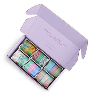 May include: A set of 10 colorful washi tapes in a purple box. The tapes feature various patterns, including geometric shapes, floral designs, and abstract patterns. The box has the text "Wherever life plants you, bloom with grace" and "Irvine, California occasionalmotif" printed on it.
