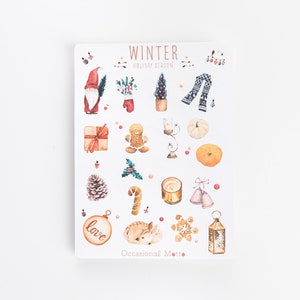 May include: A sheet of stickers with a winter holiday theme. The stickers feature illustrations of a snowman, a gingerbread man, a Christmas tree, a reindeer, a present, a candy cane, a pine cone, a pumpkin, a candle, a lantern, a snowflake, a mitten, a bell, and a Christmas ornament. The stickers are printed on white paper with a light brown border.