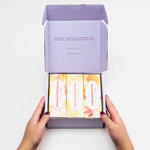 May include: A purple box containing three rolls of washi tape. The washi tape designs are "Autumn Whispers", "Fallen Silhouettes", and "Full Symphony". The box is open and the washi tape is visible. The text on the box reads "Unrolling a spectrum of creativity with every tape, where imagination meets hues. Irvine, California occasionalmatte"