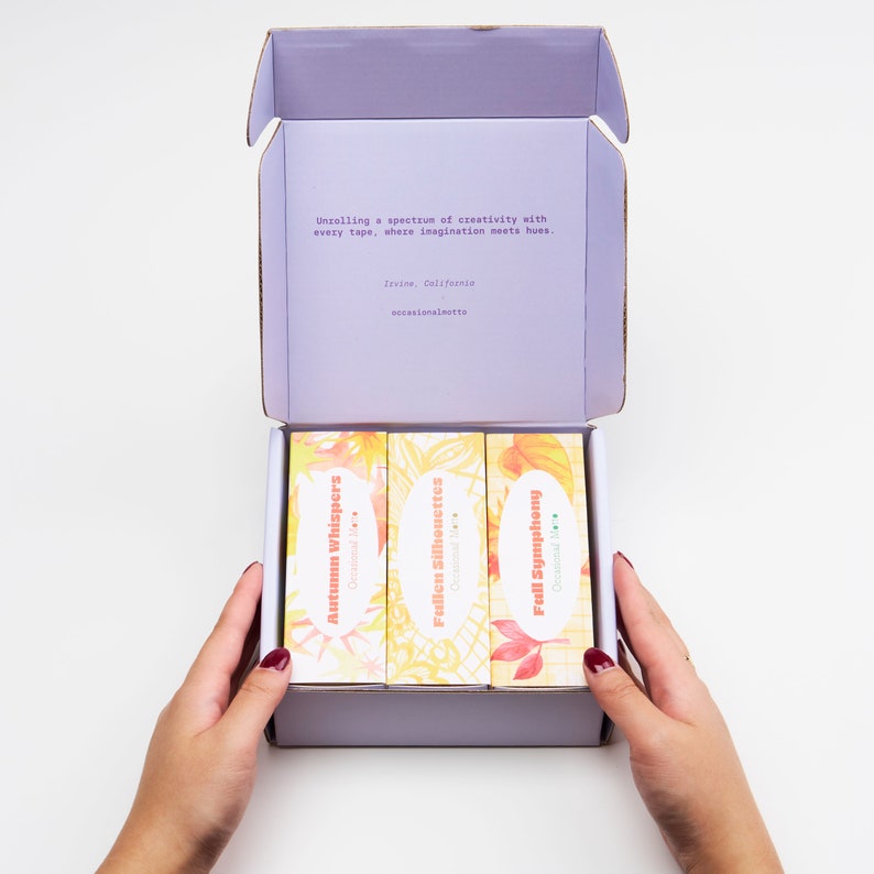 May include: A purple box containing three rolls of washi tape. The washi tape designs are "Autumn Whispers", "Fallen Silhouettes", and "Full Symphony". The box is open and the washi tape is visible. The text on the box reads "Unrolling a spectrum of creativity with every tape, where imagination meets hues. Irvine, California occasionalmatte"