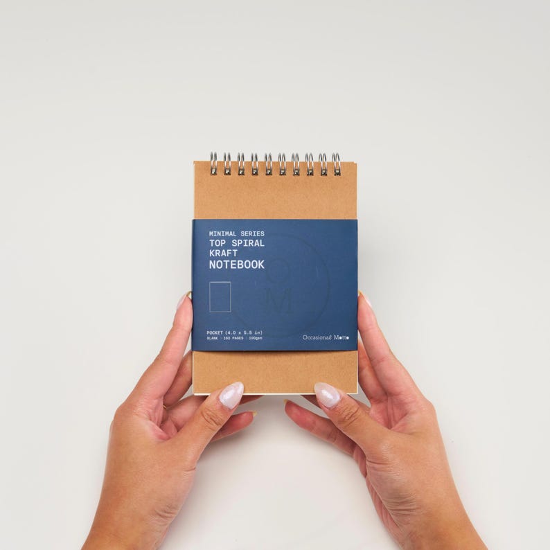 Op de afbeelding: Een bruin kraft notitieboekje met een blauwe omslag waarop "Minimal Series Top Spiral Kraft Notebook" en "Occasional Note" staat. Het notitieboekje is 4,0 x 5,8 inch en heeft 100 pagina's.
