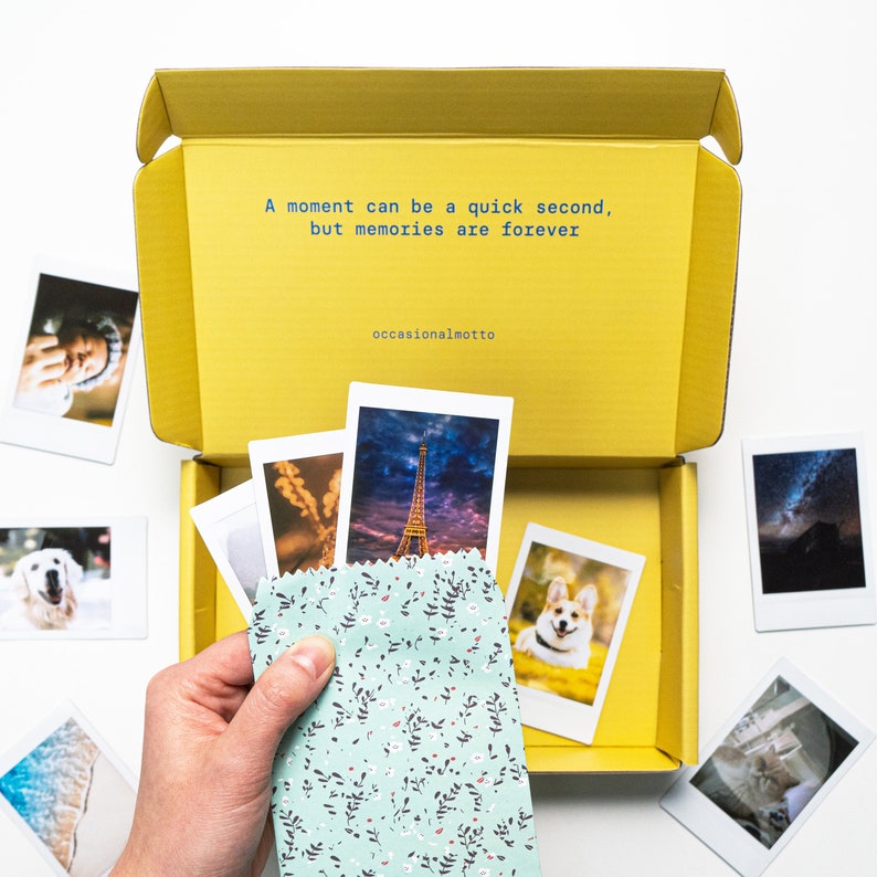 May include: A yellow box with a quote inside: "A moment can be a quick second, but memories are forever." The quote is attributed to "occasionalmotto". The box is open and contains a variety of instant photos, including a photo of the Eiffel Tower, a dog, and a landscape.