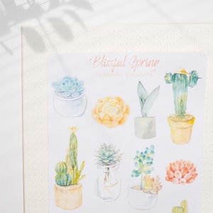 May include: A sheet of watercolor succulent stickers with the title "Blissful Spring Watercolor Succulents". The stickers feature various succulents in pots, including a cactus, a yellow flower, and a green plant with a purple leaf.
