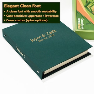 May include: A dark green binder with gold foil text on the cover reading Joyce & Zach June 1st, 2024 and the text Volume I on the spine. The binder features a clean font, metal ring mechanisms, and off-white pages visible along the side edge.