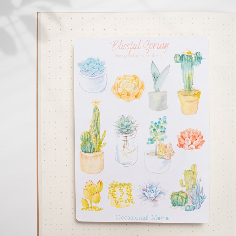 May include: A sheet of stickers featuring watercolor illustrations of succulents and cacti in various colors and styles. The stickers are titled "Blissful Spring Watercolor Succulents" and "Occasional Motto".