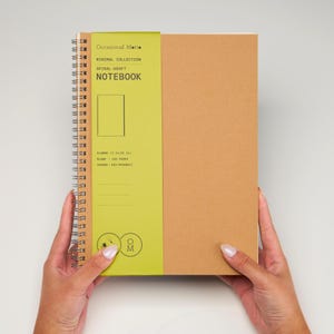 May include: A brown spiral notebook with a green spine. The spine has the text "Occasional Matte", "Minimal Collection", "Spiral-Kraft", and "Notebook". The notebook is 7.34 inches wide and has 100 pages.