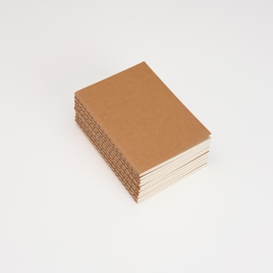 May include: A stack of rectangular notebooks with plain brown cardstock covers and visible stitched binding along the spine. The notebooks are arranged in a neat pile, showcasing the textured paper material and the exposed thread stitching.