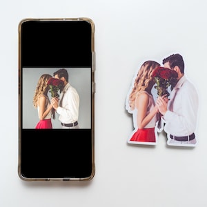 May include: A sticker of a couple kissing with a bouquet of red roses in front of their faces. The sticker is on a white background.